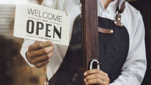 Store owner turning open sign broad through the door glass and ready to service.