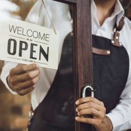 Store owner turning open sign broad through the door glass and ready to service.