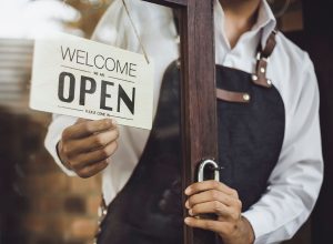 Store owner turning open sign broad through the door glass and ready to service.