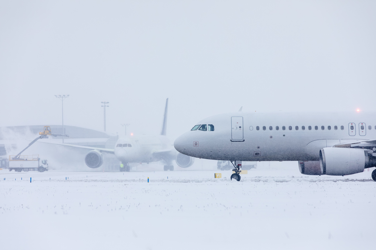 A plane sitting on a runway at an airport during a snowstorm while another plane is deiced in the background.