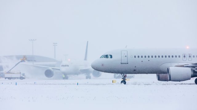 A plane sitting on a runway at an airport during a snowstorm while another plane is deiced in the background.