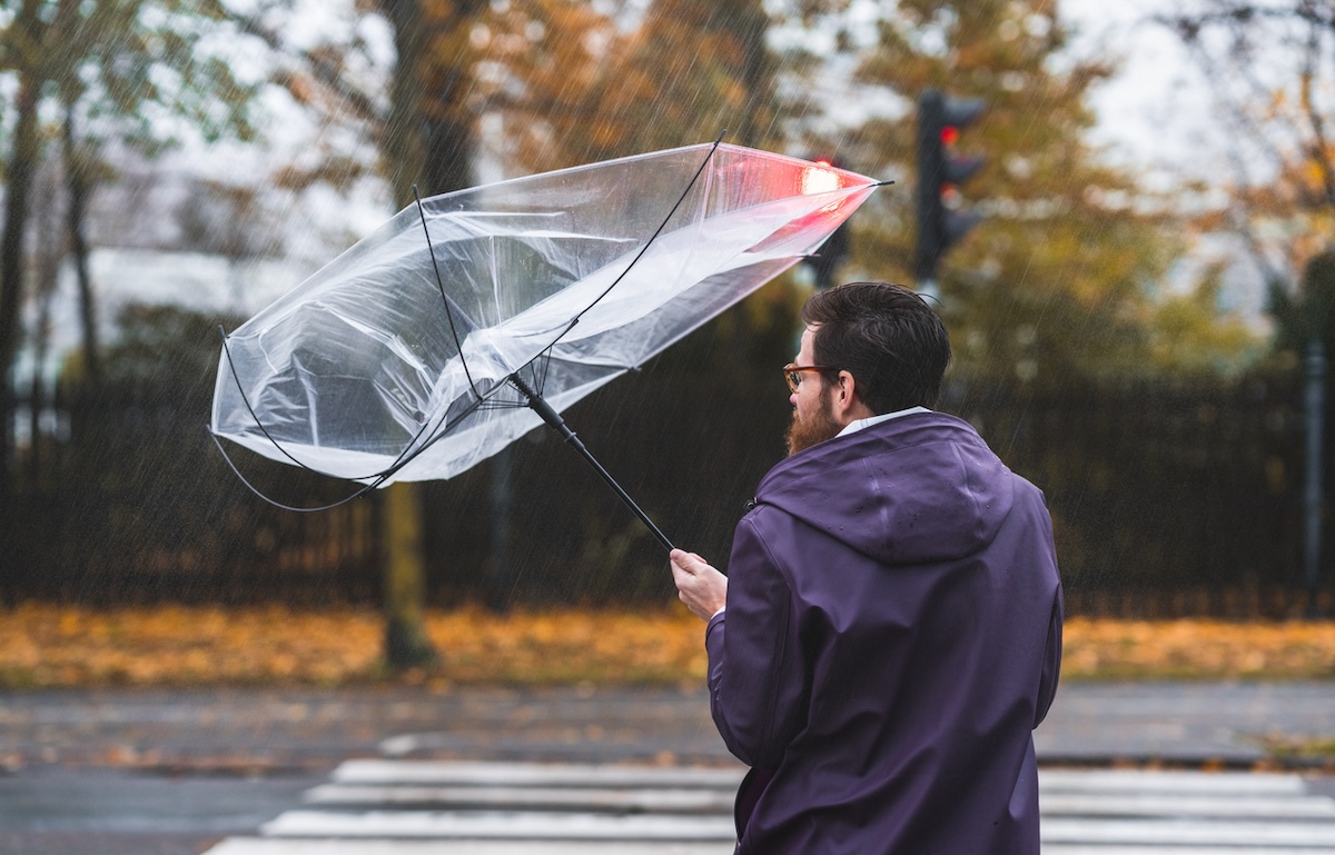 man holding an umbrella that's blowing inside out on a windy day