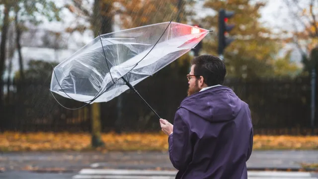 man holding an umbrella that's blowing inside out on a windy day