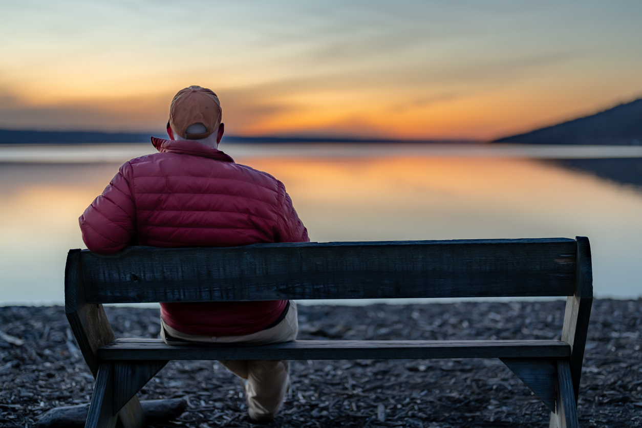 A man sitting on a bench watching a sunset over a lake