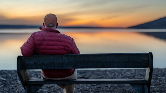 A man sitting on a bench watching a sunset over a lake