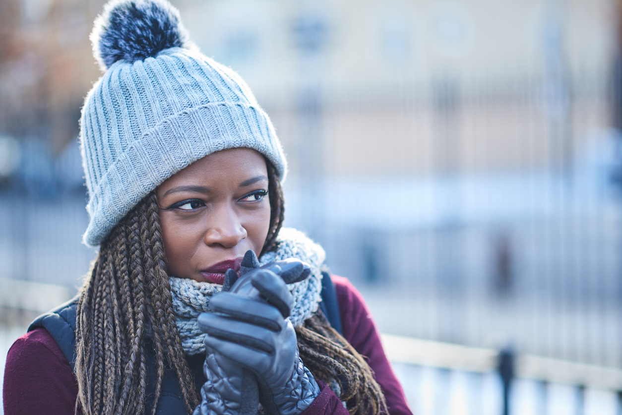 A woman wearing a hat and gloves looking cold while standing outside