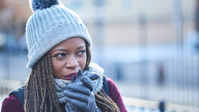 A woman wearing a hat and gloves looking cold while standing outside