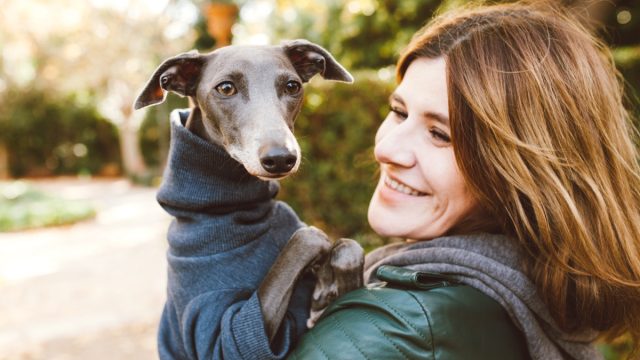 Photo of joyful woman with dog, feels fun, carries her lovely Italian Greyhound puppy, expresses affection, have good relationship, owner