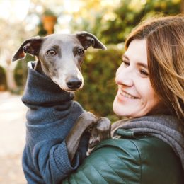 Photo of joyful woman with dog, feels fun, carries her lovely Italian Greyhound puppy, expresses affection, have good relationship, owner