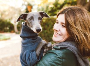 Photo of joyful woman with dog, feels fun, carries her lovely Italian Greyhound puppy, expresses affection, have good relationship, owner