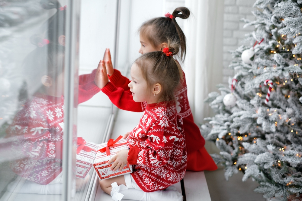 Kids sitting on a windowsill next to a Christmas tree looking out the window