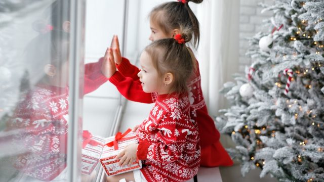 Kids sitting on a windowsill next to a Christmas tree looking out the window