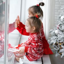 Kids sitting on a windowsill next to a Christmas tree looking out the window