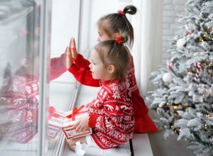 Kids sitting on a windowsill next to a Christmas tree looking out the window