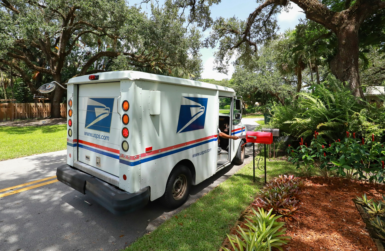 Mailman delivering mail in a postal truck puts letters into a red mailbox.