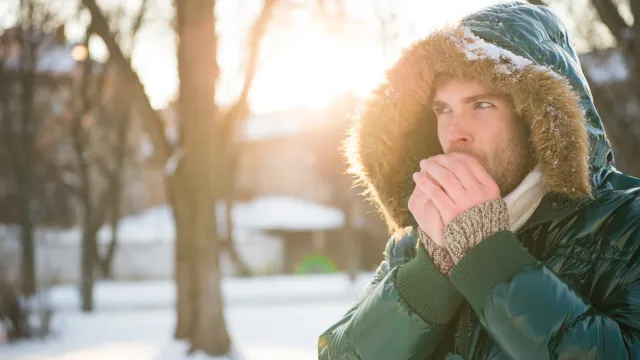 A man blowing on his hands outdoors in cold weather
