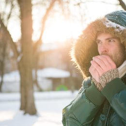 A man blowing on his hands outdoors in cold weather