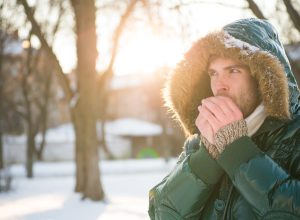 A man blowing on his hands outdoors in cold weather