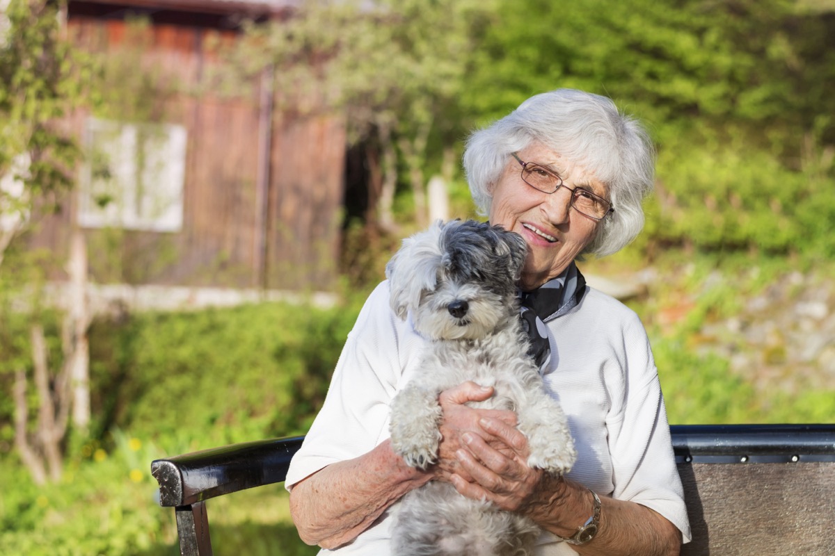 Senior woman hugging her white poodle dog in the mountain