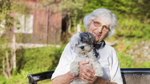 Senior woman hugging her white poodle dog in the mountain