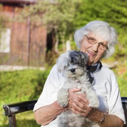 Senior woman hugging her white poodle dog in the mountain