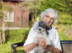 Senior woman hugging her white poodle dog in the mountain