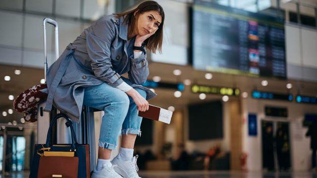 Upset woman sitting on her suitcase after her flight being canceled at the airport.