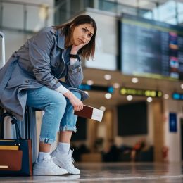 Upset woman sitting on her suitcase after her flight being canceled at the airport.