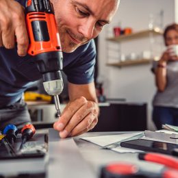 Men renovating kitchen and using cordless drill in the background standing his wife and drinking coffee