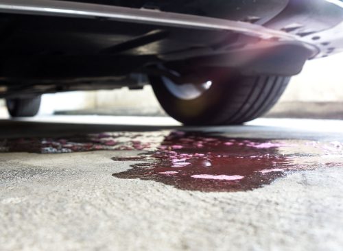 Selective focus of coolant liquid leak out from the engine down on the floor on blurred Car parked background.