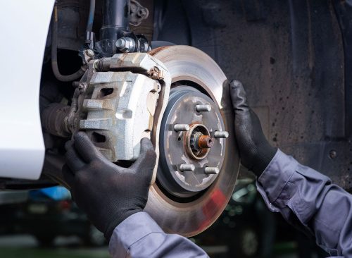 a mechanic at a car service diagnoses and replaces the caliper and brake pads in the front of the car. Car without wheels. metal spare parts. holds the brake disc with both hands