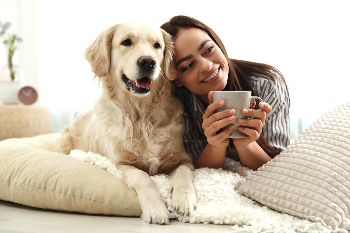 young woman drinking a cup of coffee while laying next to her golden retriever