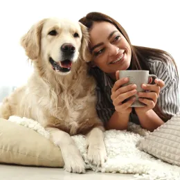 young woman drinking a cup of coffee while laying next to her golden retriever