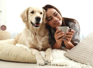 young woman drinking a cup of coffee while laying next to her golden retriever