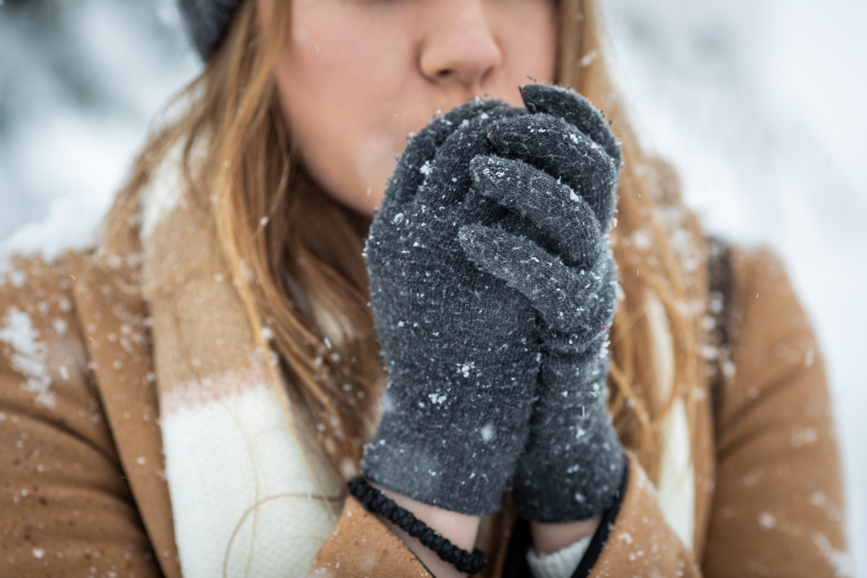 Young woman blowing arms to warm them because of the cold weather