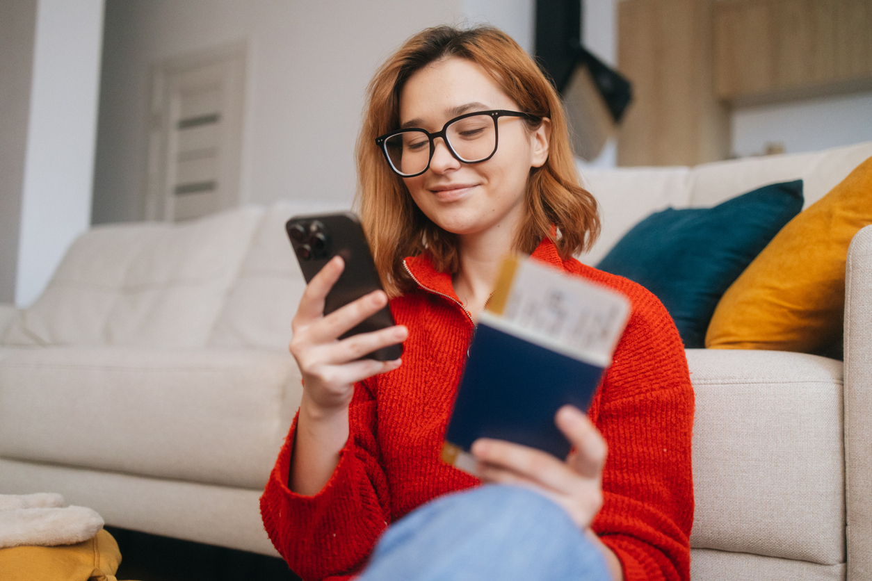 A cheerful woman uses her smartphone to make an online reservation for her holiday trip