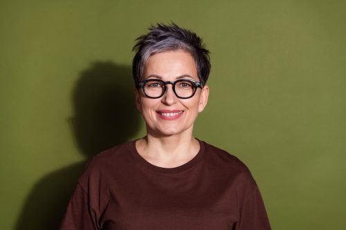 portrait of a woman with short gray hair in a brown shirt against an olive green background