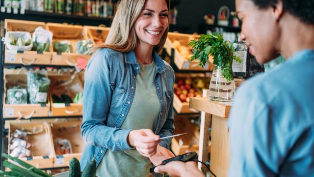 Shot of a female customer making wireless or contactless payment using debit or credit card. Woman paying for groceries at checkout in organic store.