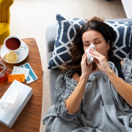 Woman is laying on a couch with a tissue in her mouth. A cup of tea is on a table next to her
