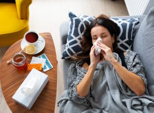 Woman is laying on a couch with a tissue in her mouth. A cup of tea is on a table next to her