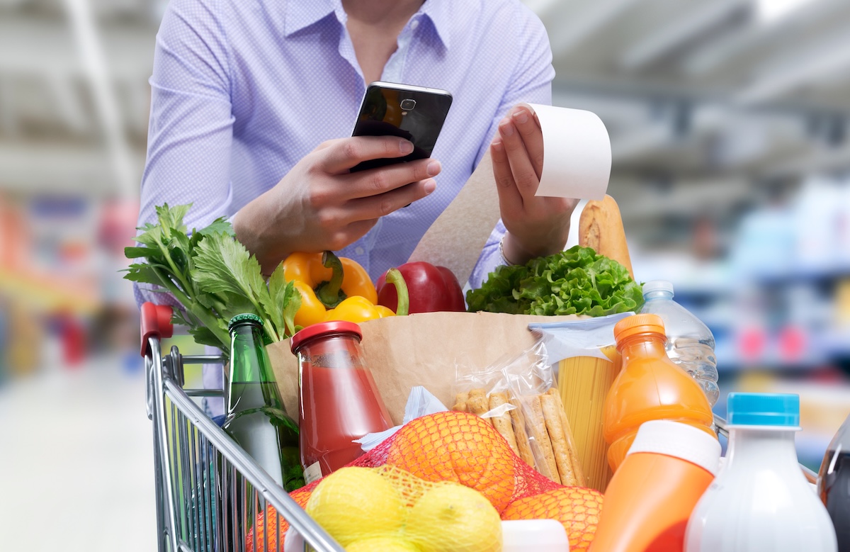 closeup of a person checking a grocery store receipt with a cart full of food