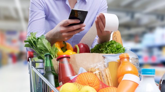 closeup of a person checking a grocery store receipt with a cart full of food