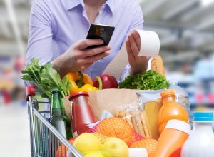 closeup of a person checking a grocery store receipt with a cart full of food
