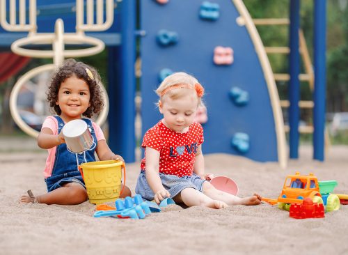 children sitting in sandbox playing with plastic colorful toys