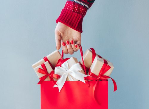 Cropped image of female hand with red polished nails holding shopping bag full of christmas gift boxes. Holiday sale concept.