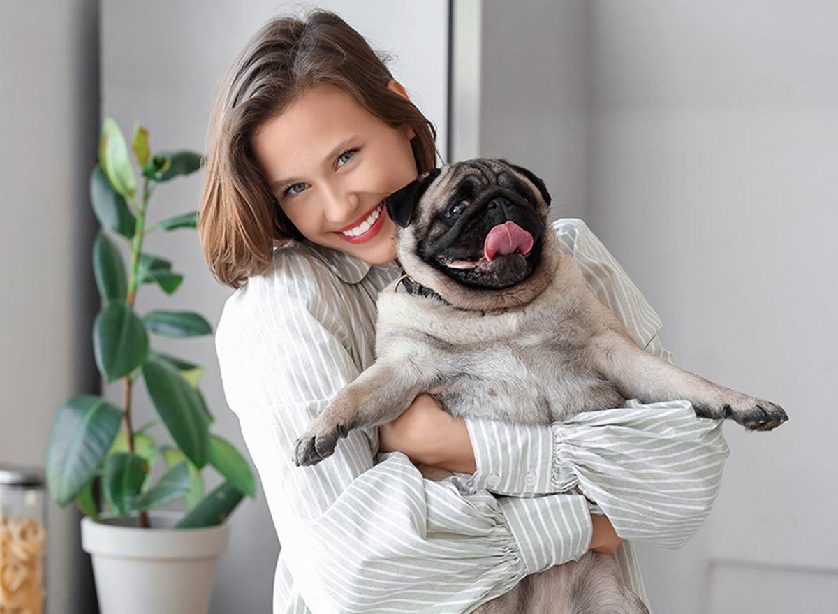 Young woman holding cute pug dog at home