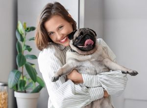 Young woman holding cute pug dog at home