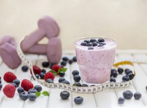 blueberry smoothie next to a measuring tape and a purple set of hand weights