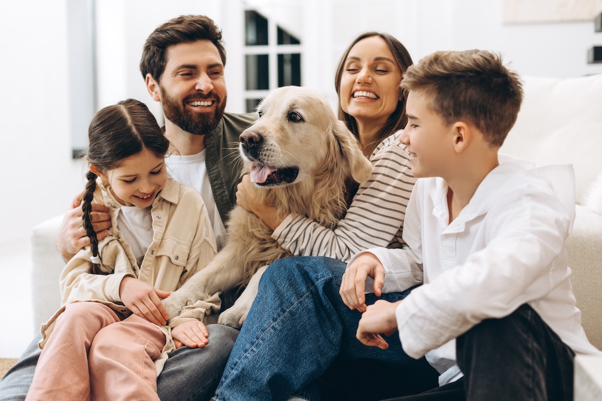 Cheerful family of four, including parents and children, enjoying quality time together while embracing their golden retriever in a cozy home setting