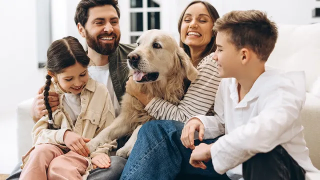 Cheerful family of four, including parents and children, enjoying quality time together while embracing their golden retriever in a cozy home setting